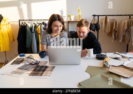 Hipster designers work on laptop with clothes patterns in tailoring atelier. Tailors team in studio Stock Photo