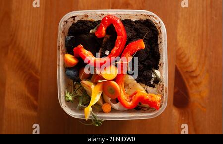 the green trash can in a plastic box on a wooden table with some rest of coffee grounds, red and yellow peppers, carrots. Stock Photo