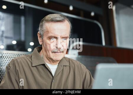 Content senior Caucasian man with mustache sitting in cafe with wifi and analyzing internet data on computer Stock Photo