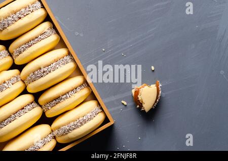Cornstarch alfajores with milk caramel and coconut in a wooden box on a light blue background. Stock Photo