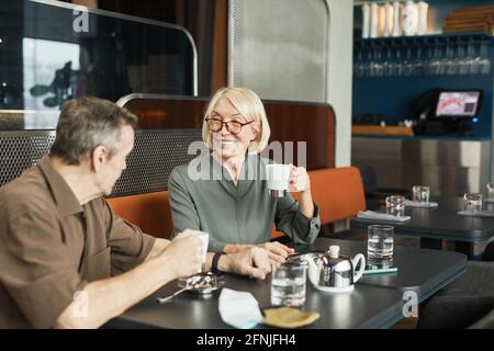 Positive senior Caucasian couple sitting at table with teapot and drinking tea while chatting in cafe Stock Photo