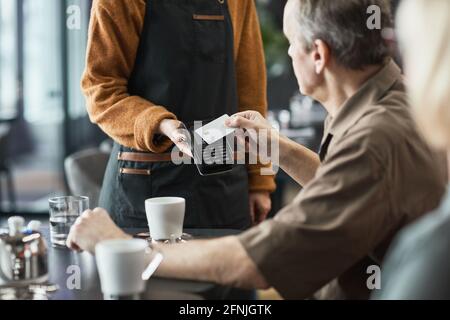 Senior man using contactless card while paying for bill through terminal with NFC in cafe Stock Photo
