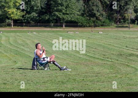 Man with prosthetic leg sitting in the chair in the field in summer, talking on mobile phone in NYC Stock Photo
