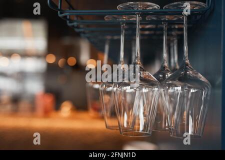Close-up of beautiful wineglasses hanging upside down on glass drying rack in bar or pub Stock Photo