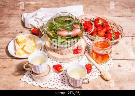https://l450v.alamy.com/450v/2fnjp6j/teatime-concept-aromatic-mint-tea-ripe-strawberries-sweet-honey-a-hot-drink-ceramic-cups-on-stands-vintage-linen-napkin-old-wooden-boards-backg-2fnjp6j.jpg