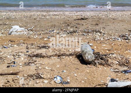 An old, semi-decomposed plastic bottle lies on the seashore among shells and sand. Environmental pollution concept. Dirty sea. Ecological problem. Cop Stock Photo