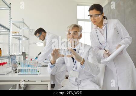 Two male and female scientists analyze samples working with chemicals in a laboratory. Stock Photo