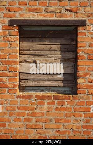 Closed with wooden planks window opening in an old red brick wall. Stock Photo
