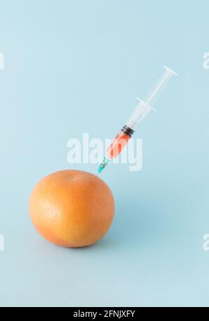 A red grapefruit on which stands a syringe that has extracted fresh juice on a blue background. Fruit Summer vitamin concept. Minimal style. Stock Photo