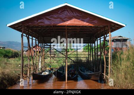 Four long traditional wooden boats in a simple garage on bamboo stilts in a canal near Inle Lake, Nyaung Shwe, Shan state, Myanmar Stock Photo