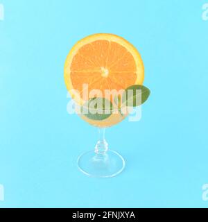 A glass filled with orange juice and decorated with a slice of orange and green leaves on a blue background. Summer refreshing citrus drink. Simple co Stock Photo