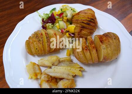 Lunch with baked potatoes, salad and fried fish on white plate, ready to eat. Stock Photo