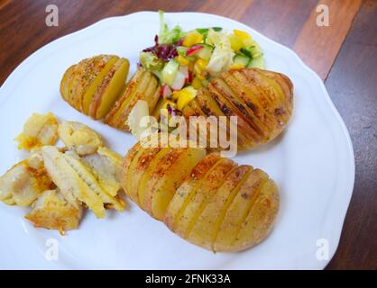 Lunch with baked potatoes, salad and fried fish on white plate, ready to eat. Stock Photo