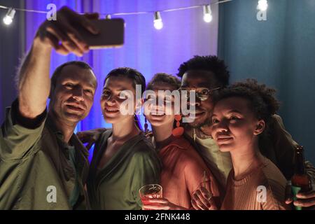 Diverse group of friends taking selfie or video chatting together during indoor party at home Stock Photo