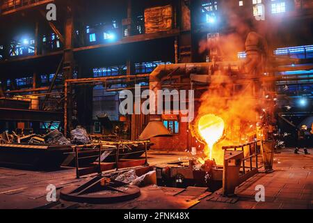 Pouring molten metal into mold from ladle container in foundry metallurgical factory workshop, iron cast, heavy industrial background. Stock Photo