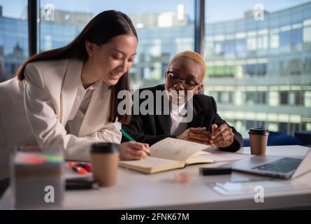 Positive diverse businesswoman making notes in office Stock Photo
