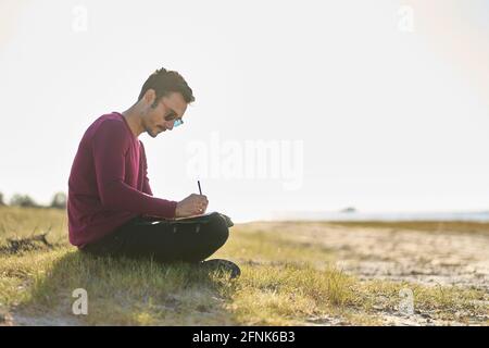 young man writing on the beach Stock Photo