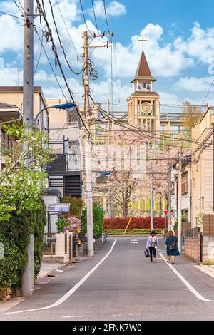 tokyo, japan - april 07 2021: Street lined by cherry trees below the bell tower of the Seigakuin Junior & Senior High School overlooked by a christian Stock Photo