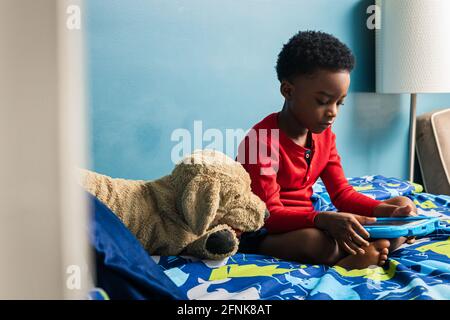 Boy using digital tablet while sitting by toy dog on bed at home Stock Photo