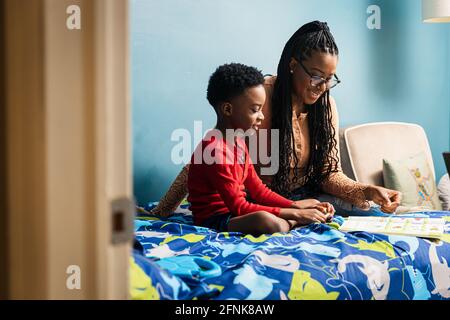Mother assisting son studying in bedroom at home Stock Photo