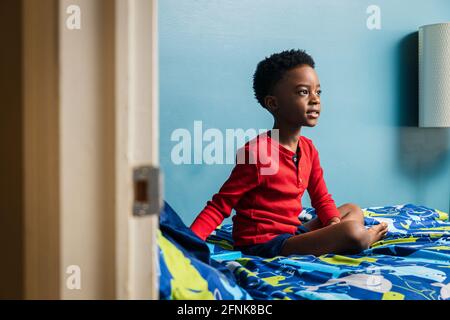 Thoughtful boy looking away while sitting on bed at home Stock Photo