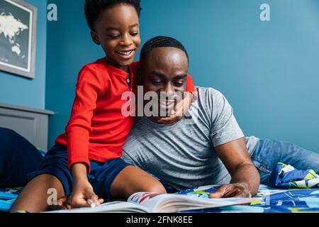 Father and son having fun doing homework on bed at home Stock Photo