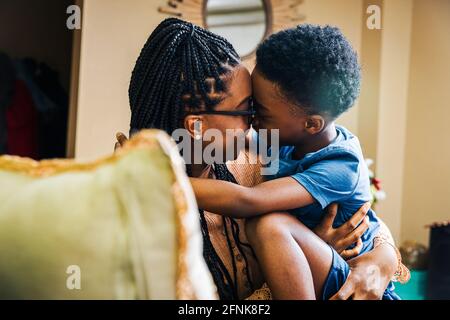 Playful boy embracing mother while sitting in living room at home Stock Photo