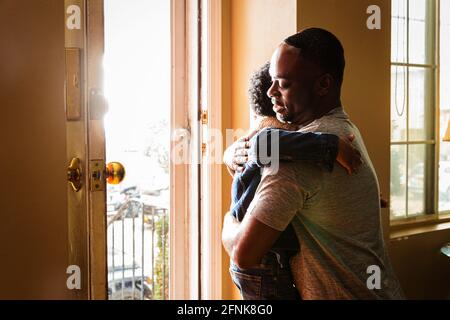 Son embracing father at entrance of home Stock Photo