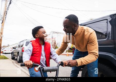 Smiling father teaching happy son to ride a bike outside at home Stock Photo