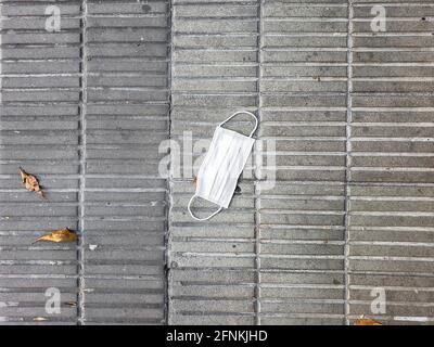 Covid mask on slated brick ground with fallen dry leaves next to it Stock Photo