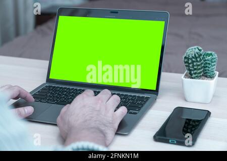 Young businessman working on laptop in home, rear view green screen of business man hands busy using laptop at office desk, typing on computer sitting Stock Photo