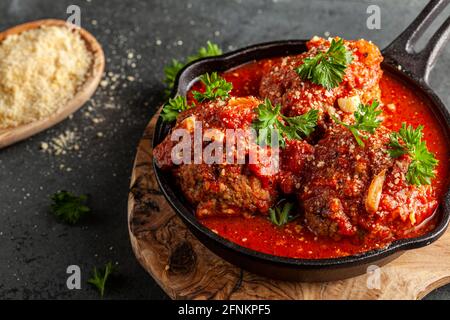 Close up view of three traditional large Italian meatballs in sizzling tomato sauce in cast iron pan. The pan sits on wooden trivet and parsley leaves Stock Photo