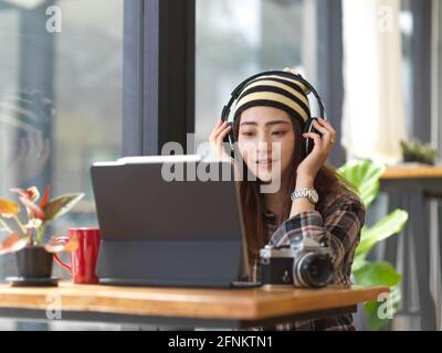 Young female photographer listening to the music through headphones while taking a rest from work Stock Photo