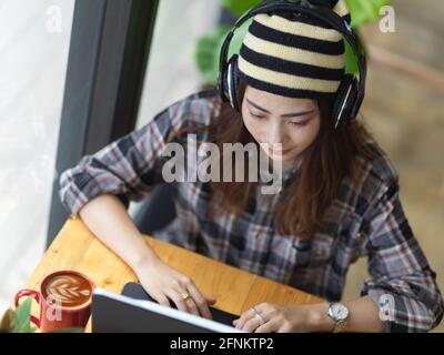 Overhead shot of female teenager with headphone working with tablet in cafe Stock Photo