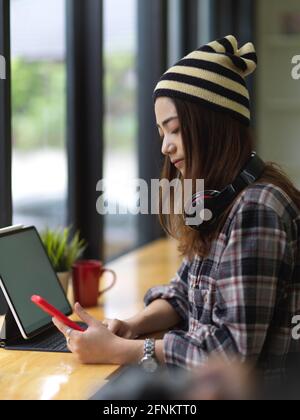 Side view of young beautiful woman using smartphone while working with tablet Stock Photo