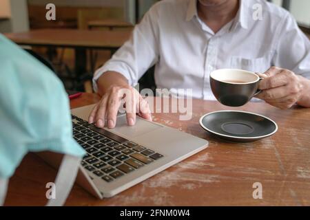 Businessman touching mouse pad on computer laptop and holding cup of tea with another hand. Stock Photo