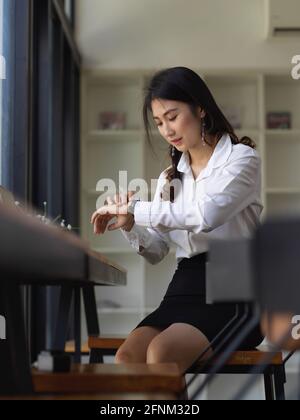 Young professional businesswoman checking the time on her watch while sitting on the office room Stock Photo