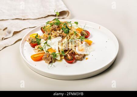 Close-up of delicious homemade spaghetti with vegetables, cheese and fried quail eggs on a round plate on a light background. Traditional Italian food Stock Photo