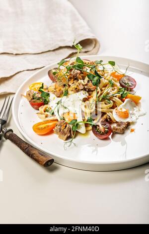 Close-up of delicious homemade spaghetti with vegetables, cheese and fried quail eggs on a round plate on a light background. Traditional Italian food Stock Photo