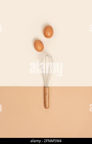 Two brown Eggs and whisk with wooden handle on beige background. Flat lay Top view Concept. Stock Photo