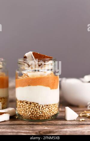 Layered breakfast or dessert with puffed quinoa grains, yogurt and coconut flakes and pieces in glasses Stock Photo