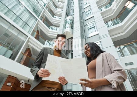 Low angle view of young architects examining blueprints together while standing outdoors with modern building in the background Stock Photo