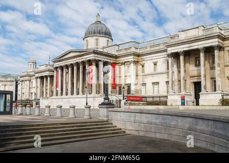Two people outside the National Gallery taken from Trafalgar Square. One person sitting on a wall wearing a face mask, the other walking away. Stock Photo