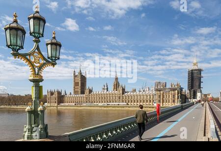 Houses of Parliament from across Westminster Bridge.A few Pedestrians are wearing face masks and traffic is visible at the far end of the bridge. Stock Photo