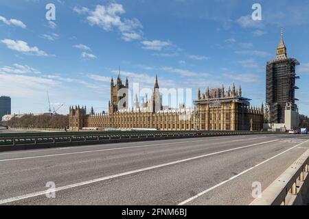 Houses of Parliament from Westminster Bridge, which is clear of people and traffic, although some people are visible at the far end the bridge. Stock Photo
