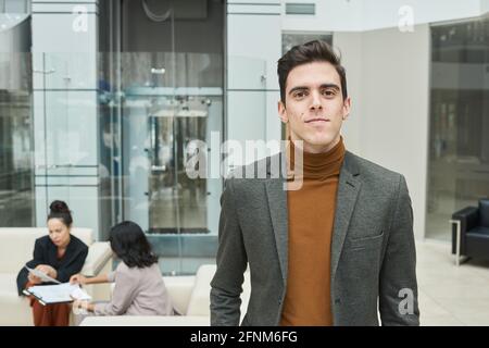 Portrait of young businessman looking at camera with two businesswomen in the background Stock Photo