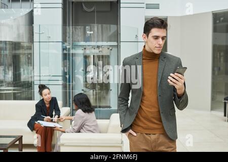 Young businessman using his mobile phone with two businesswomen communicating in the background Stock Photo