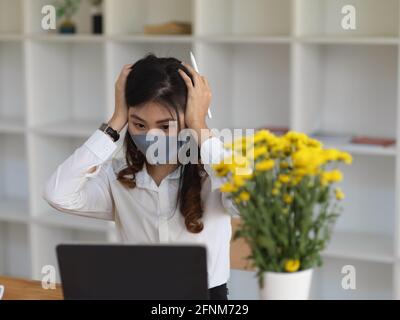 Portrait of female worker wearing mask feeling stressed while working in office room Stock Photo