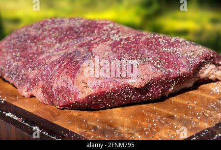 Large portion of seasoned tender lean raw beef brisket for roasting standing ready for cooking on a wooden chopping board in a close up low angle Stock Photo