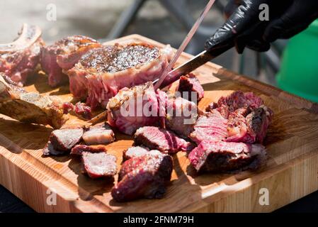 Chef de-boning and carving a portion of barbecued prime rib steak with a large knife in a close up low angle on the meat on a wooden cutting board Stock Photo
